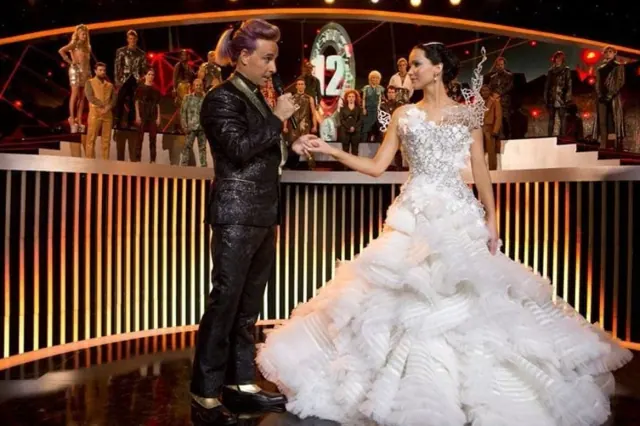 Jennifer Lawrence as Katniss wearing a large ruffled white gown on the interview stage