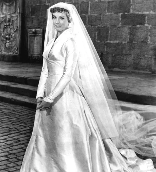 Julie Andrews as Maria in a full-skirted wedding gown outside a stone church doorway