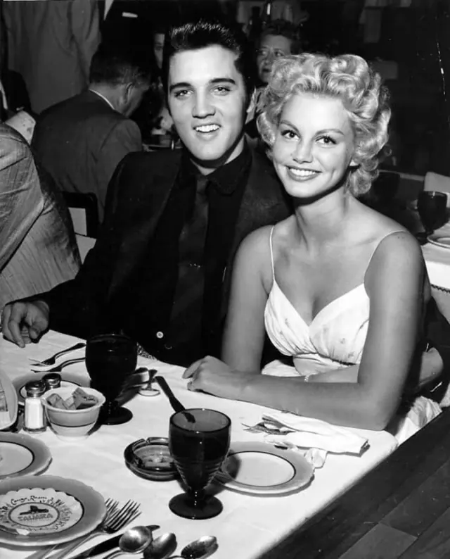 Elvis seated at a table beside a woman