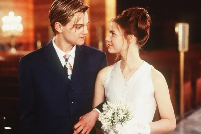 Claire Danes as Juliet wearing a simple pale bridal dress and gloves beside Leonardo DiCaprio