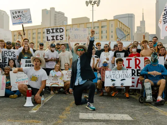 Crowd holding homemade signs at a Birds Aren't Real event