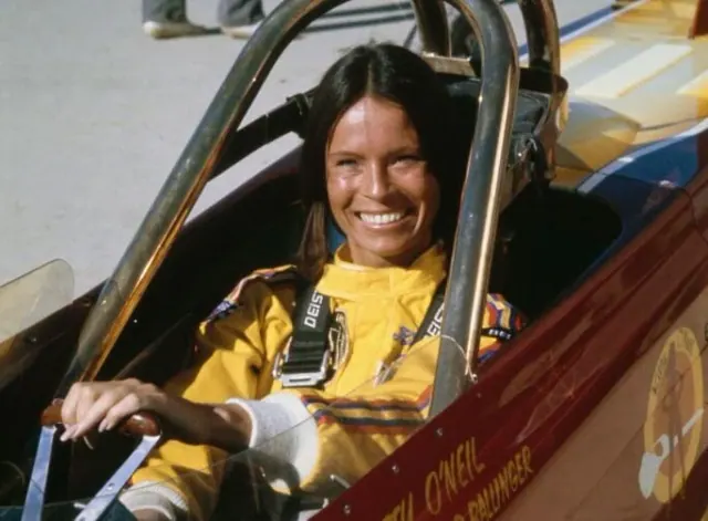 Kitty O'Neil smiling while seated in a racing vehicle.