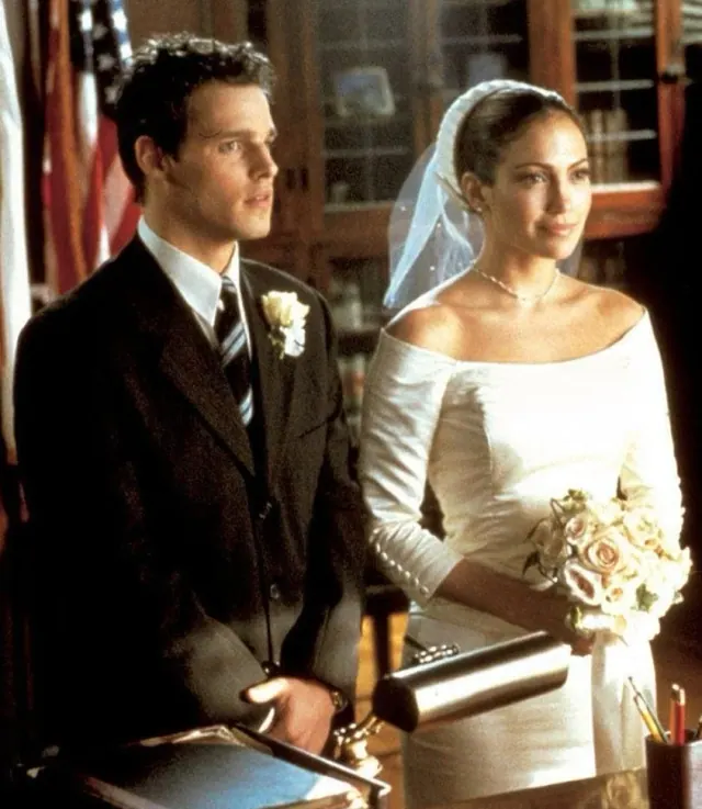 Jennifer Lopez as Mary in a fitted white dress and veiled cap beside Justin Chambers as Massimo