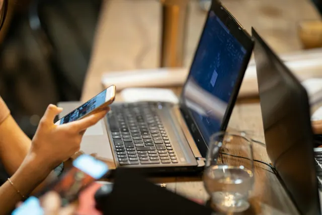 Person looking at a phone beside an open laptop