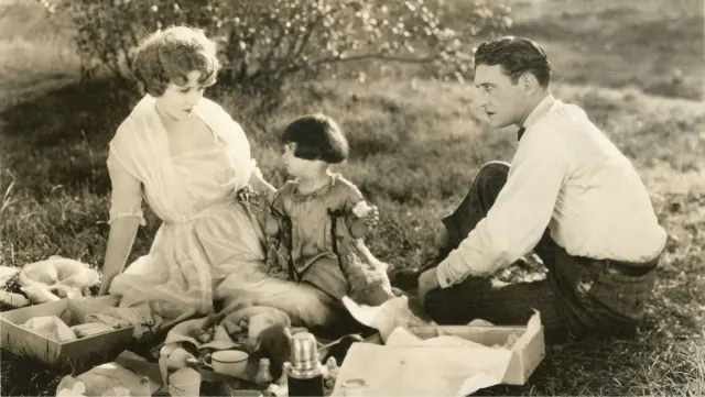 Baby Peggy seated outdoors between adult actors in an archive still from Fools First.