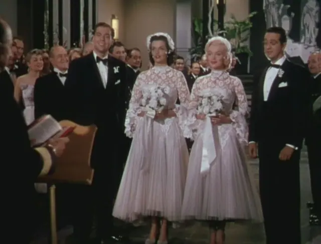 Marilyn Monroe and Jane Russell wearing matching lace wedding outfits and small veiled hats