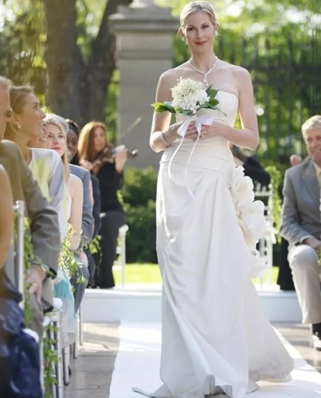 Kelly Rutherford as Lily in a sleeveless draped wedding dress at an outdoor ceremony
