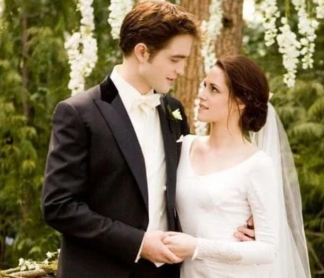 Kristen Stewart as Bella wearing a long-sleeved gown beside Robert Pattinson as Edward