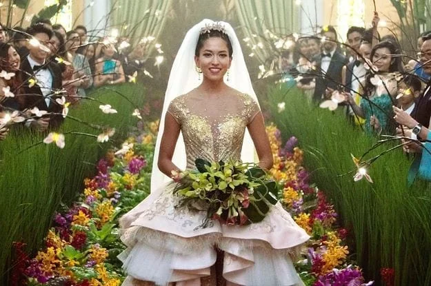 Sonoya Mizuno as Araminta wearing a decorated bridal outfit in a flower-lined wedding aisle